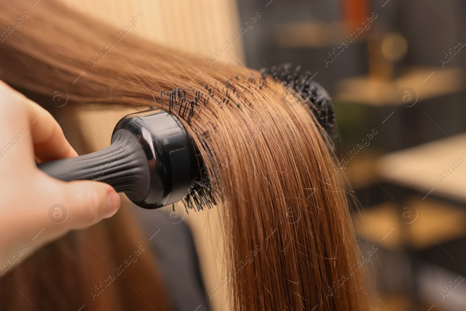 Photo of Hairdresser styling client's hair with round brush in salon, closeup