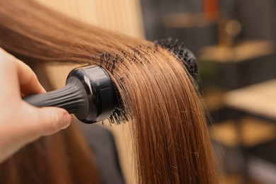 Photo of Hairdresser styling client's hair with round brush in salon, closeup