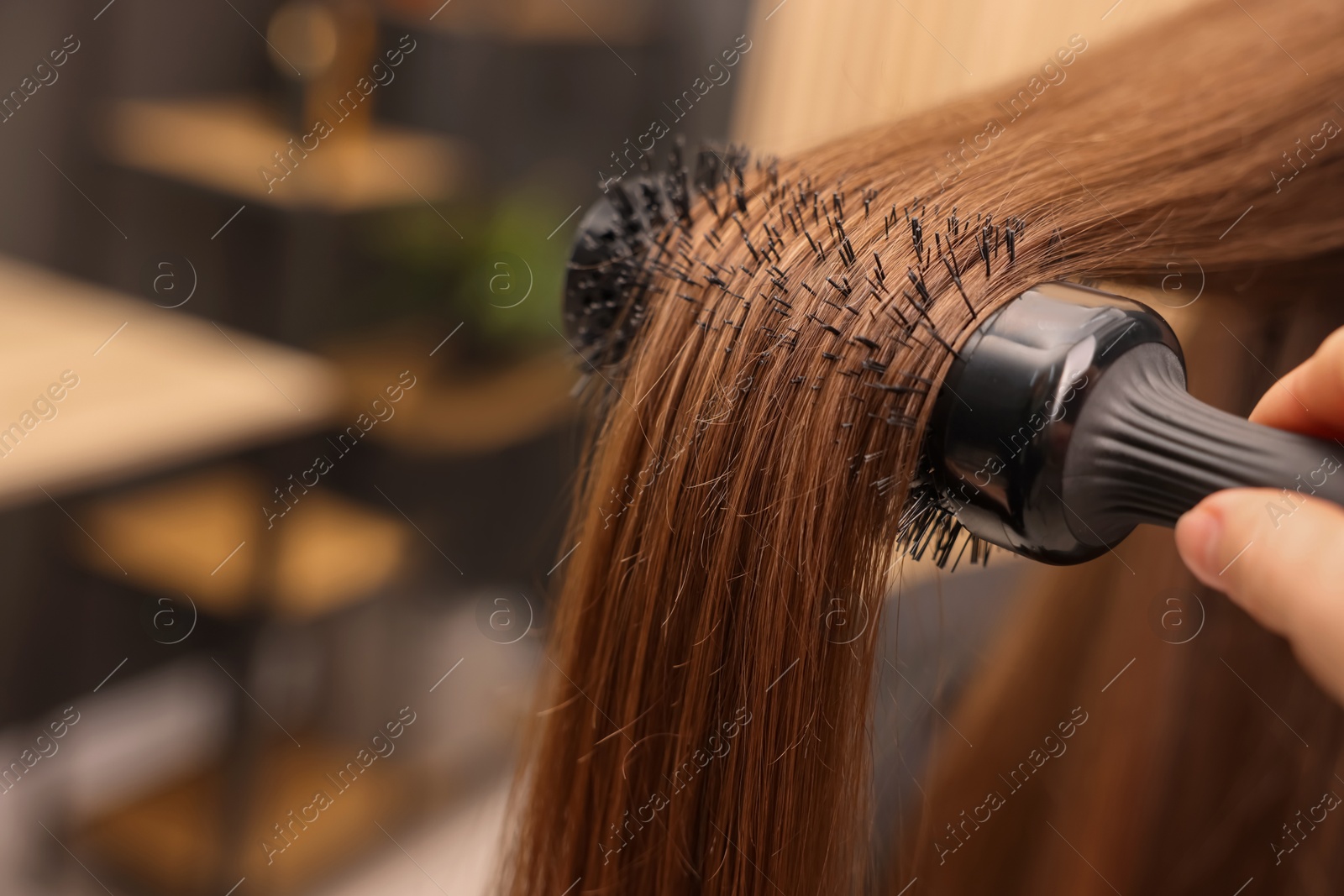 Photo of Hairdresser styling client's hair with round brush in salon, closeup