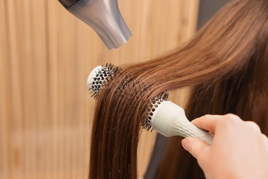 Photo of Hairdresser styling client's hair with round brush and hairdryer in salon, closeup