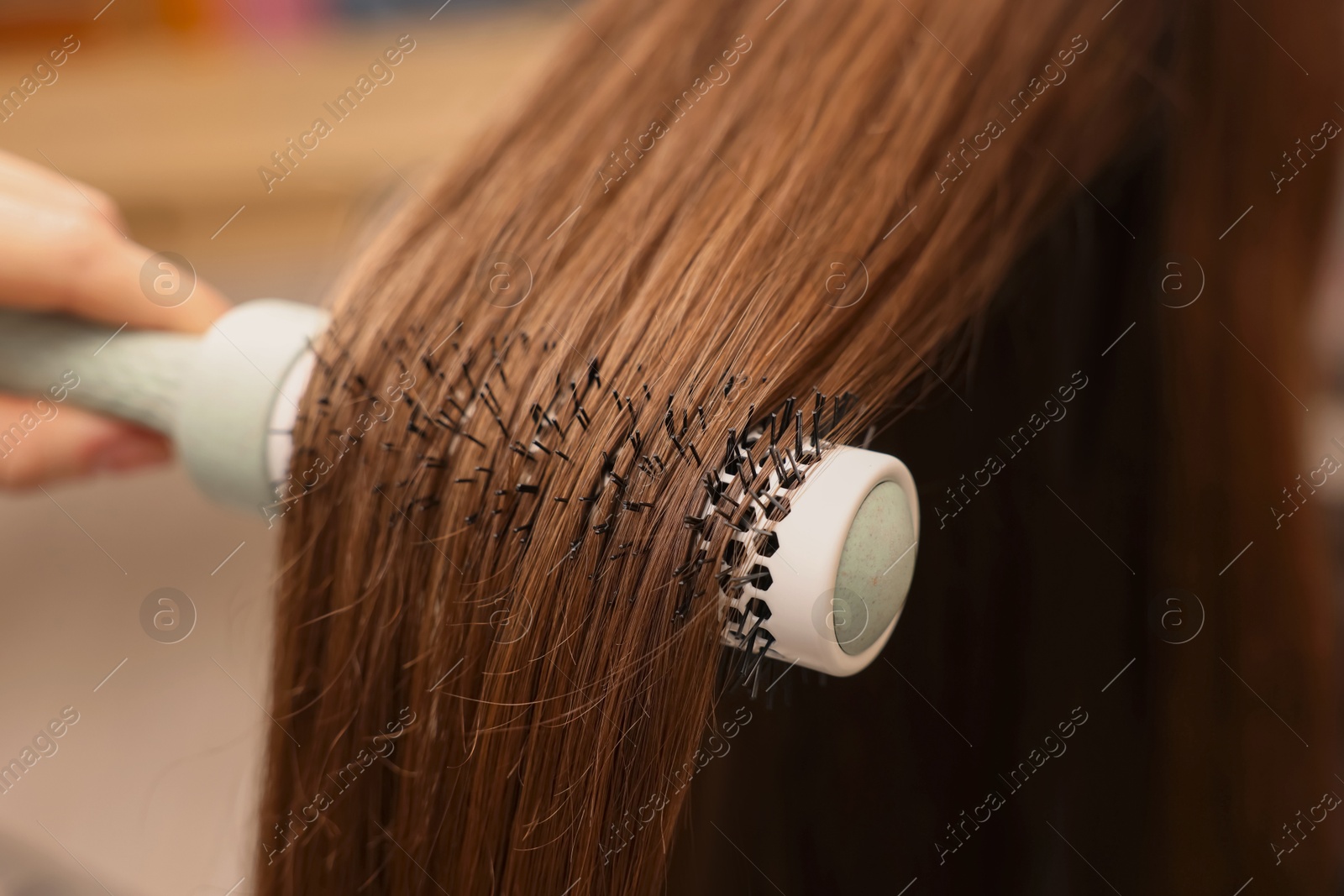 Photo of Hairdresser styling client's hair with round brush in salon, closeup