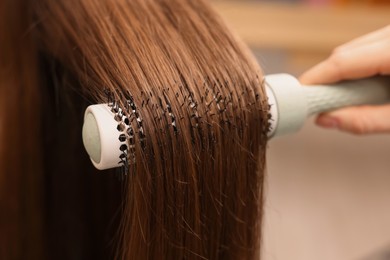 Photo of Hairdresser styling client's hair with round brush in salon, closeup