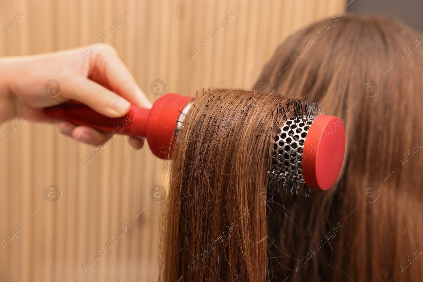 Photo of Hairdresser styling client's hair with round brush in salon, closeup