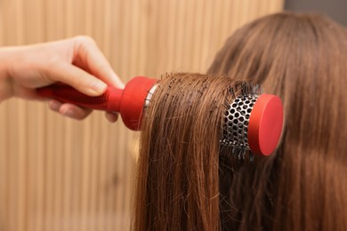 Photo of Hairdresser styling client's hair with round brush in salon, closeup