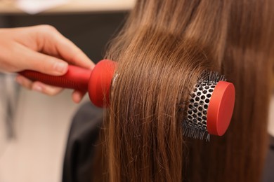 Photo of Hairdresser styling client's hair with round brush in salon, closeup