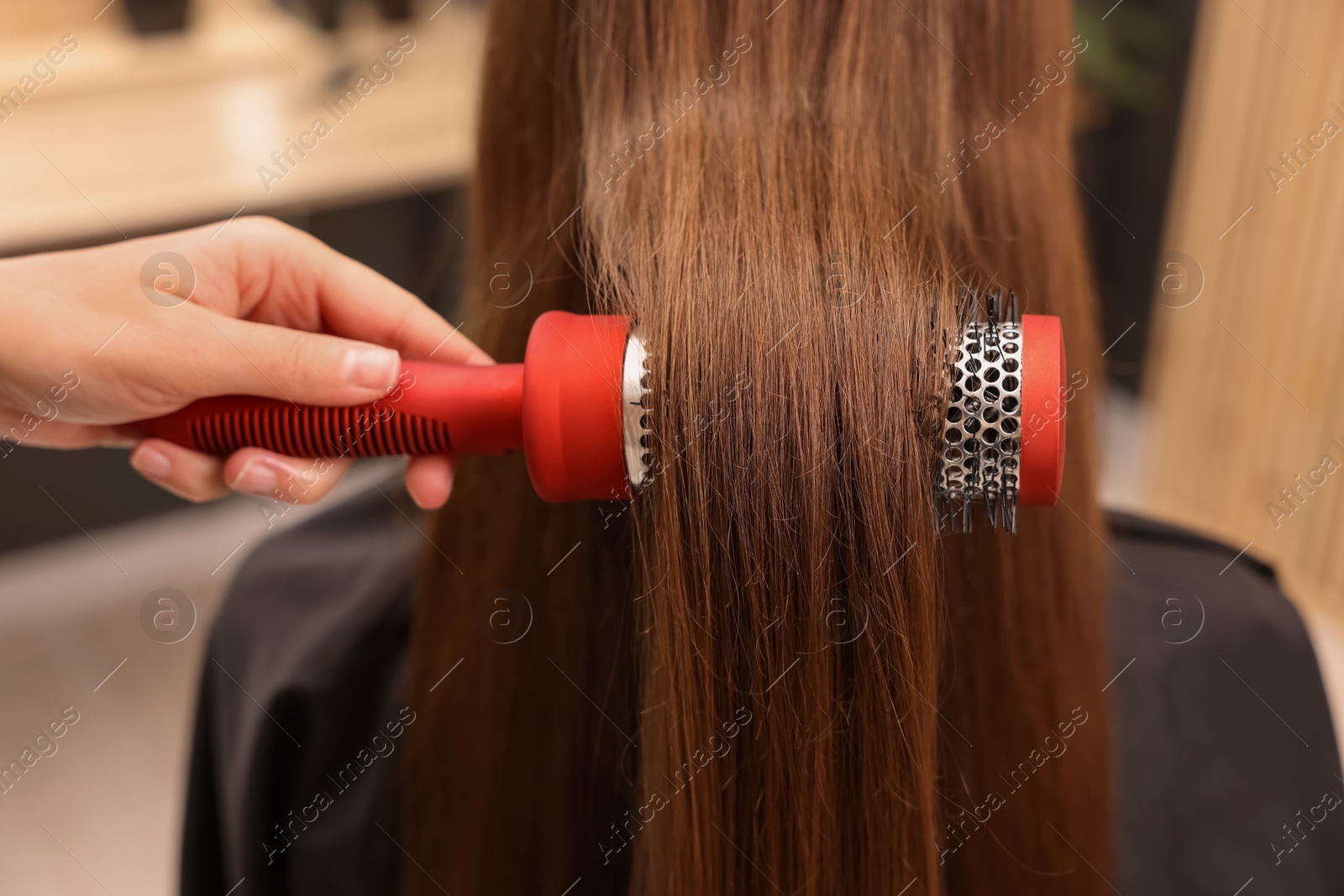 Photo of Hairdresser styling client's hair with round brush in salon, closeup