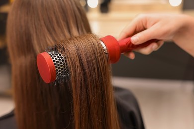 Photo of Hairdresser styling client's hair with round brush in salon, closeup