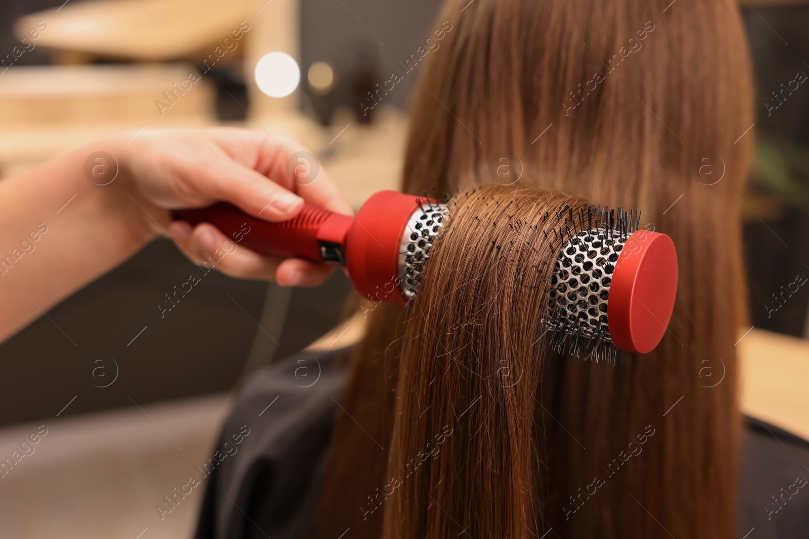 Photo of Hairdresser styling client's hair with round brush in salon, closeup