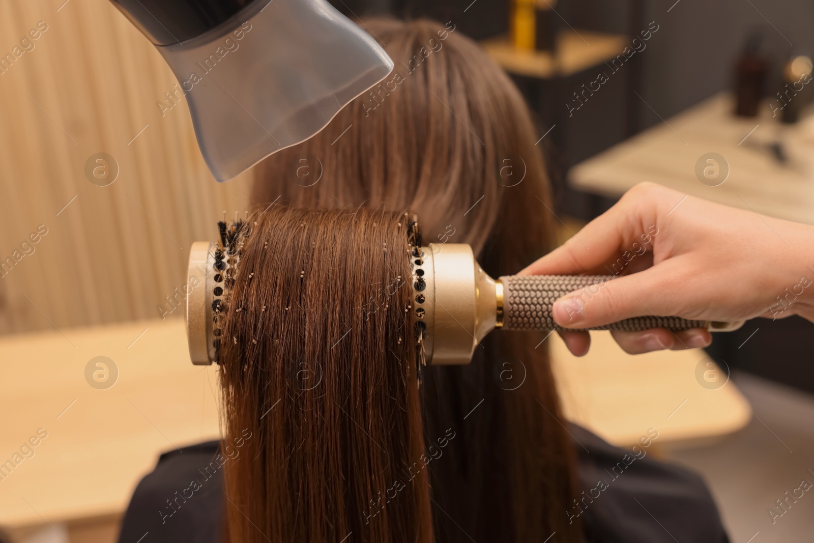 Photo of Hairdresser styling client's hair with round brush and hairdryer in salon, closeup