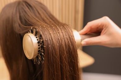 Photo of Hairdresser styling client's hair with round brush in salon, closeup