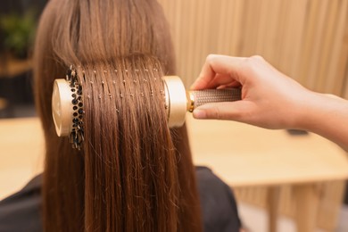 Photo of Hairdresser styling client's hair with round brush in salon, closeup