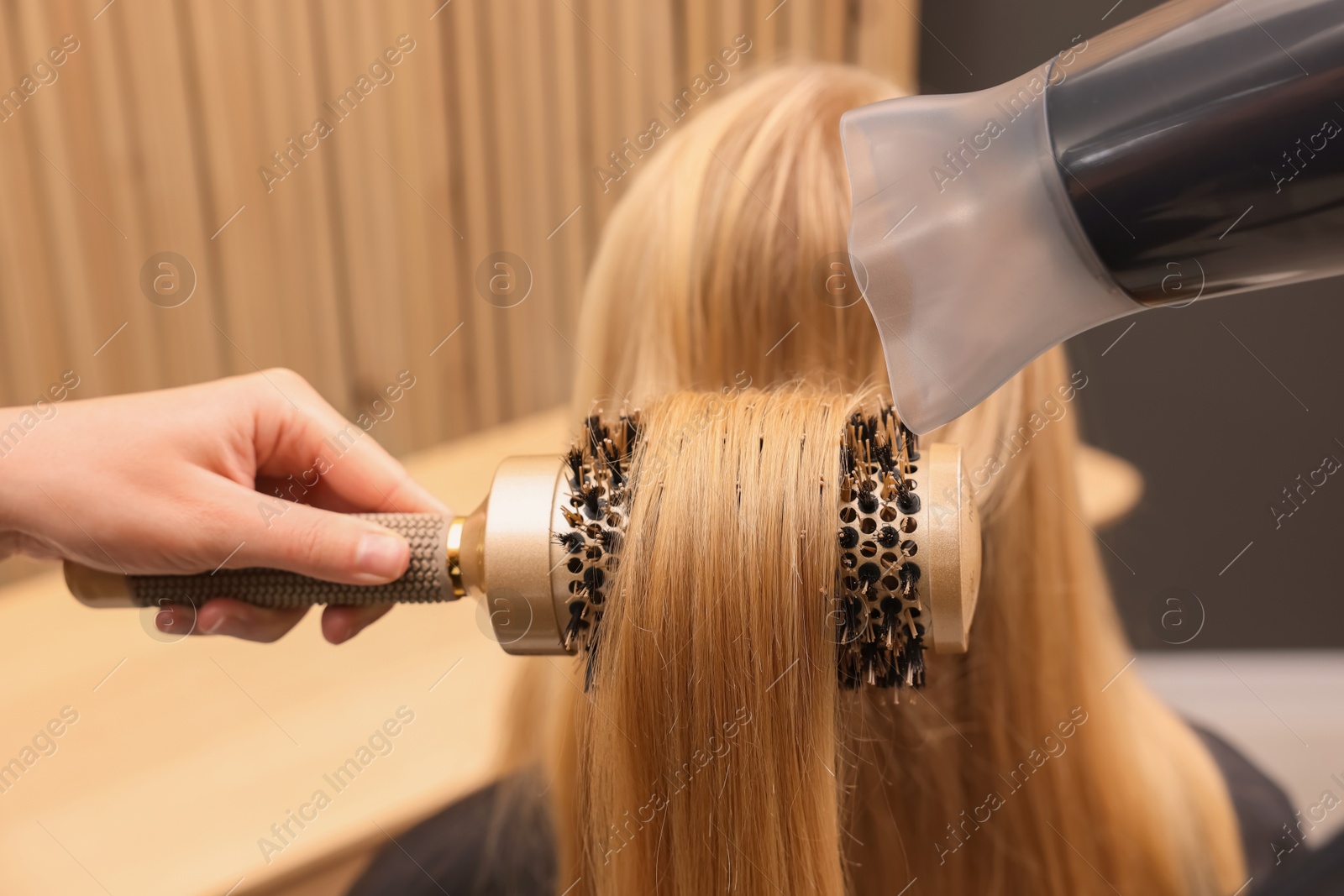 Photo of Hairdresser styling client's hair with round brush in salon, closeup