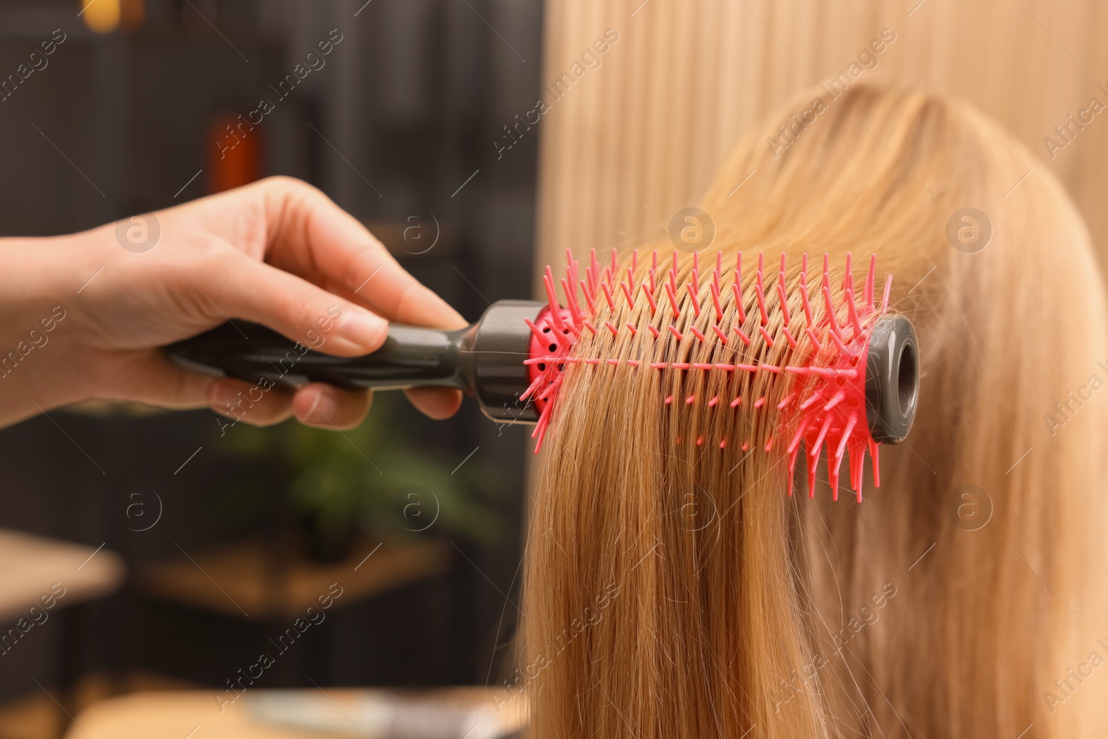 Photo of Hairdresser styling client's hair with round brush in salon, closeup