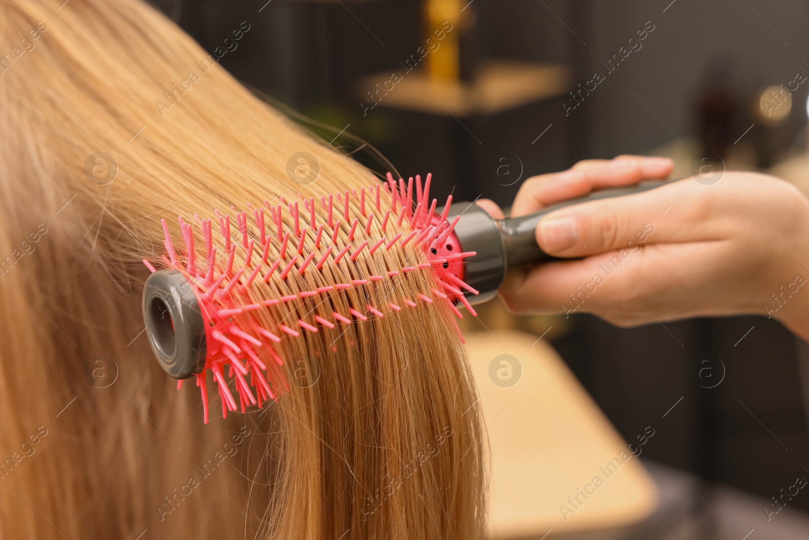 Photo of Hairdresser styling client's hair with round brush in salon, closeup