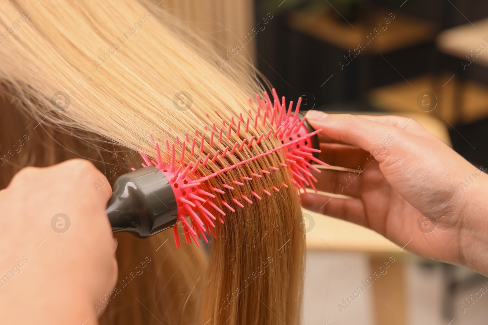 Photo of Hairdresser styling client's hair with round brush in salon, closeup