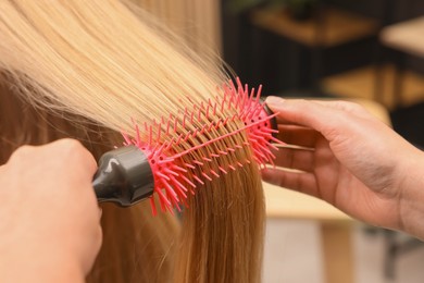 Photo of Hairdresser styling client's hair with round brush in salon, closeup