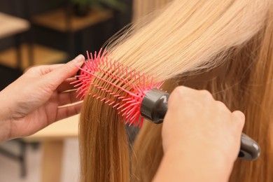 Photo of Hairdresser styling client's hair with round brush in salon, closeup