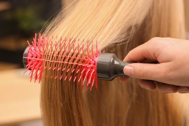 Photo of Hairdresser styling client's hair with round brush in salon, closeup