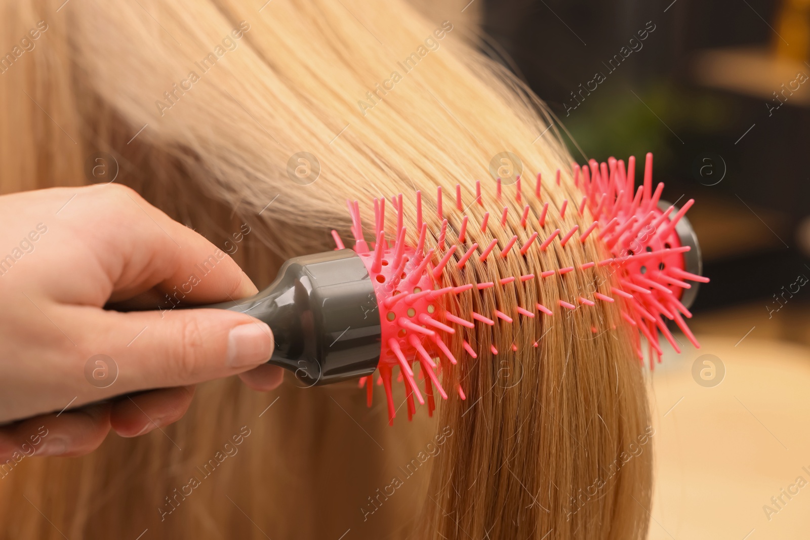 Photo of Hairdresser styling client's hair with round brush in salon, closeup