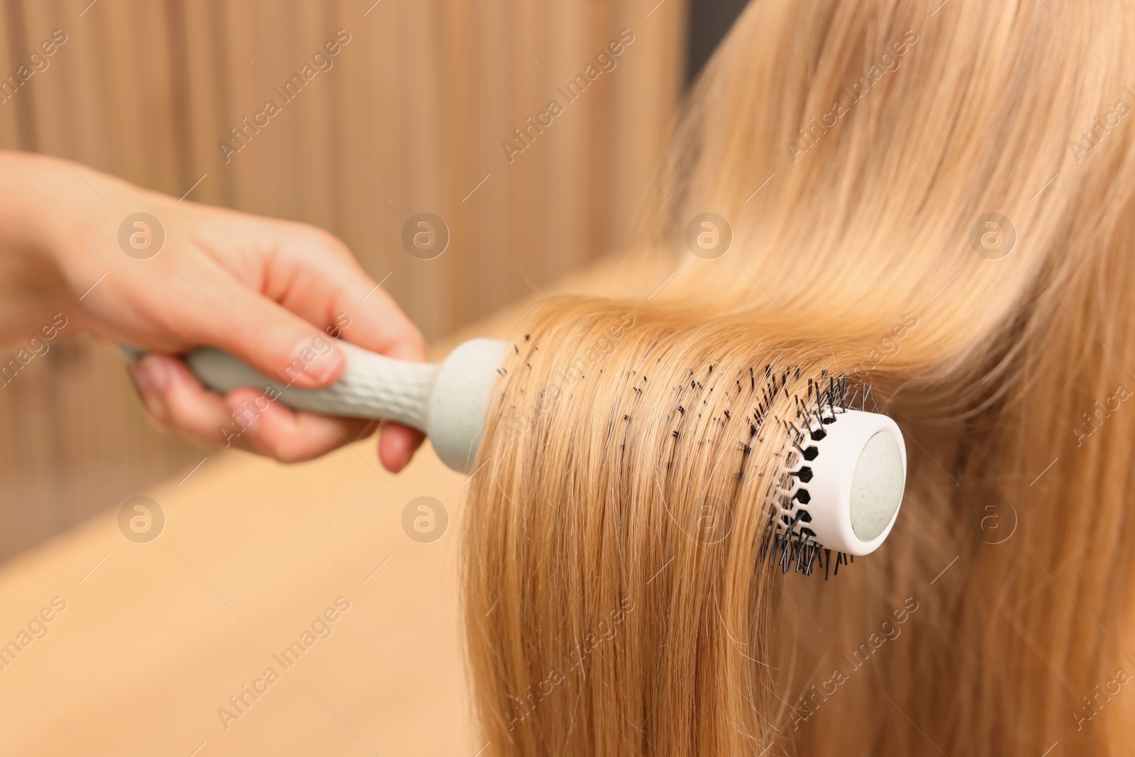 Photo of Hairdresser styling client's hair with round brush in salon, closeup