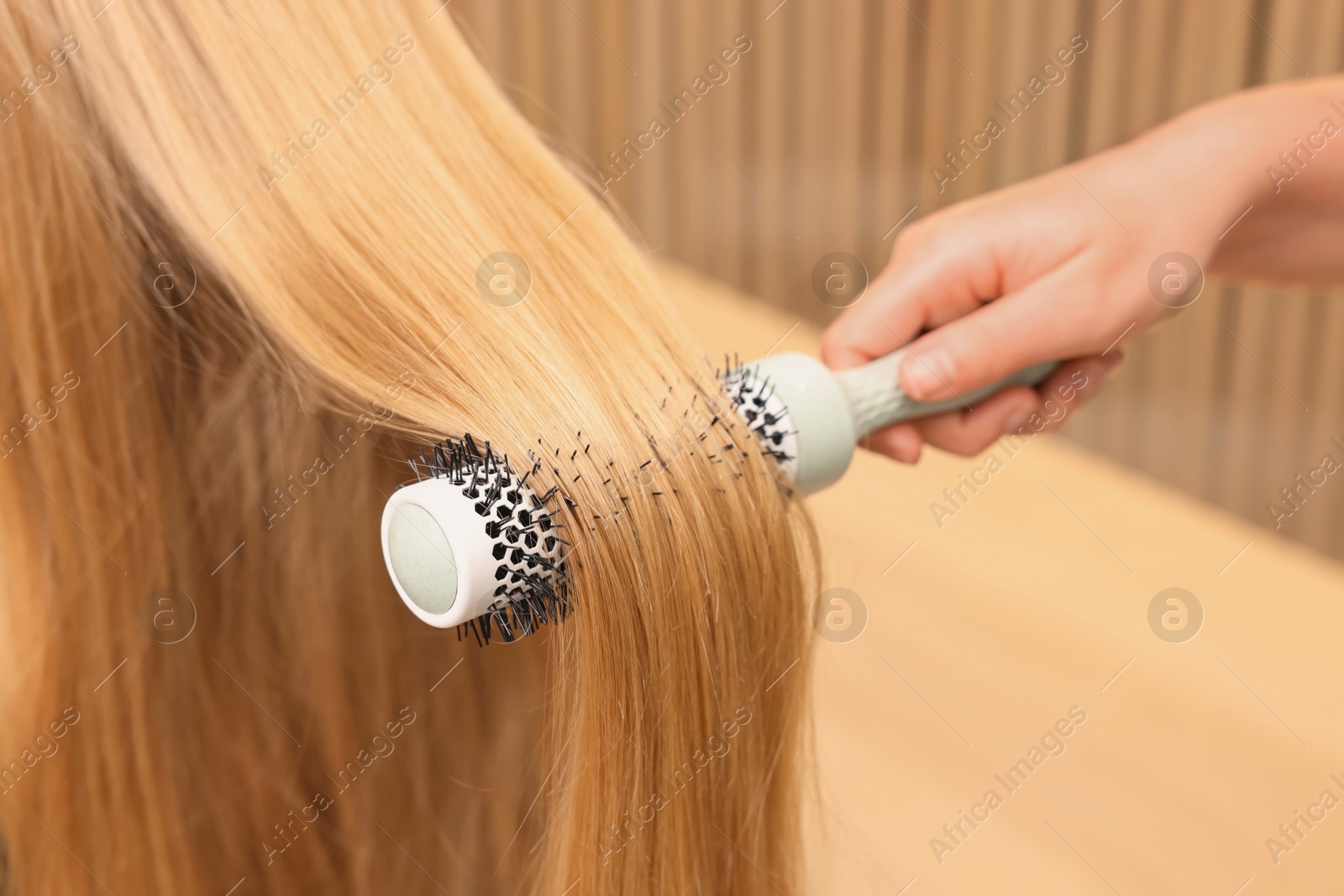 Photo of Hairdresser styling client's hair with round brush in salon, closeup