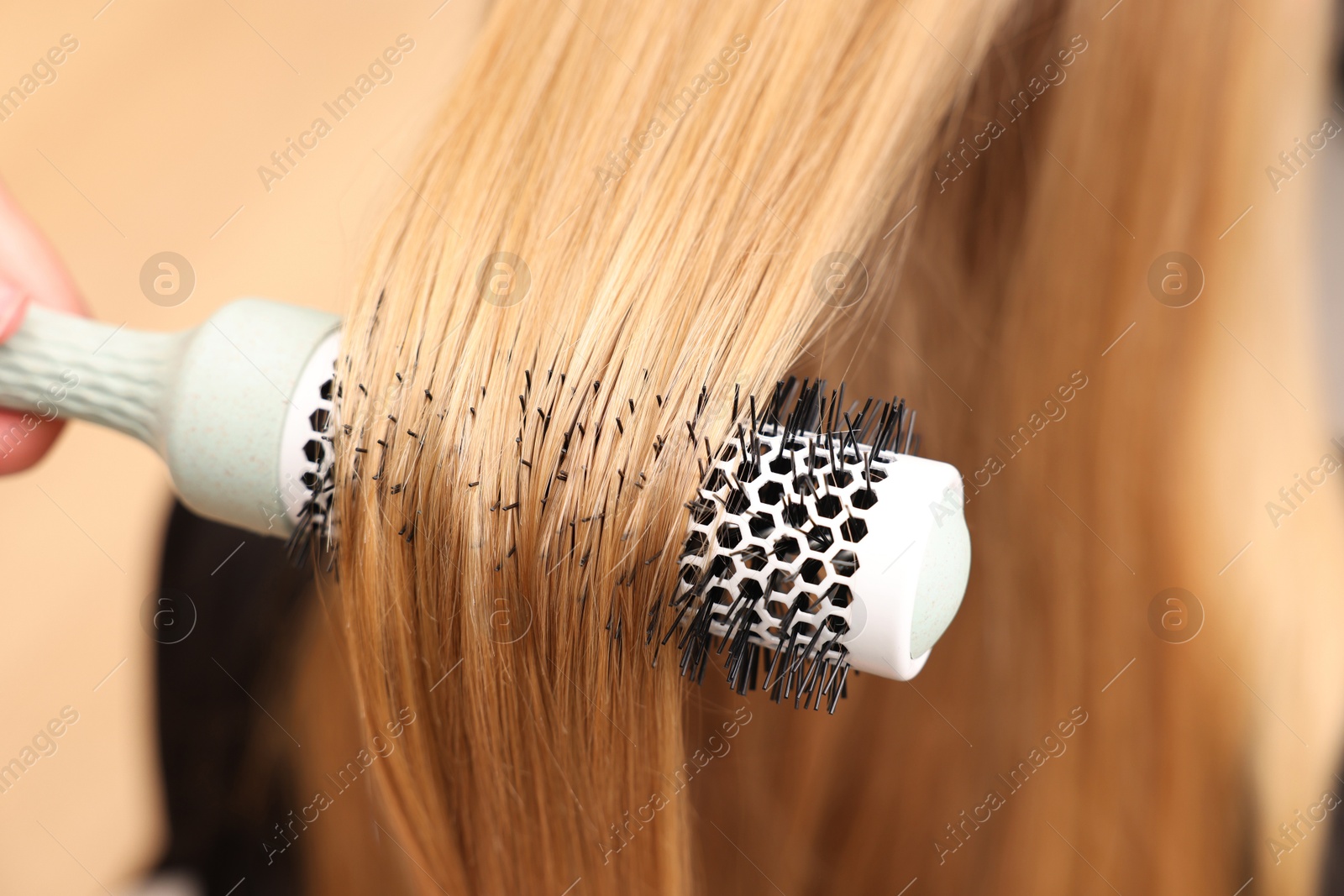 Photo of Hairdresser styling client's hair with round brush in salon, closeup