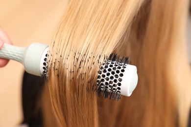 Photo of Hairdresser styling client's hair with round brush in salon, closeup