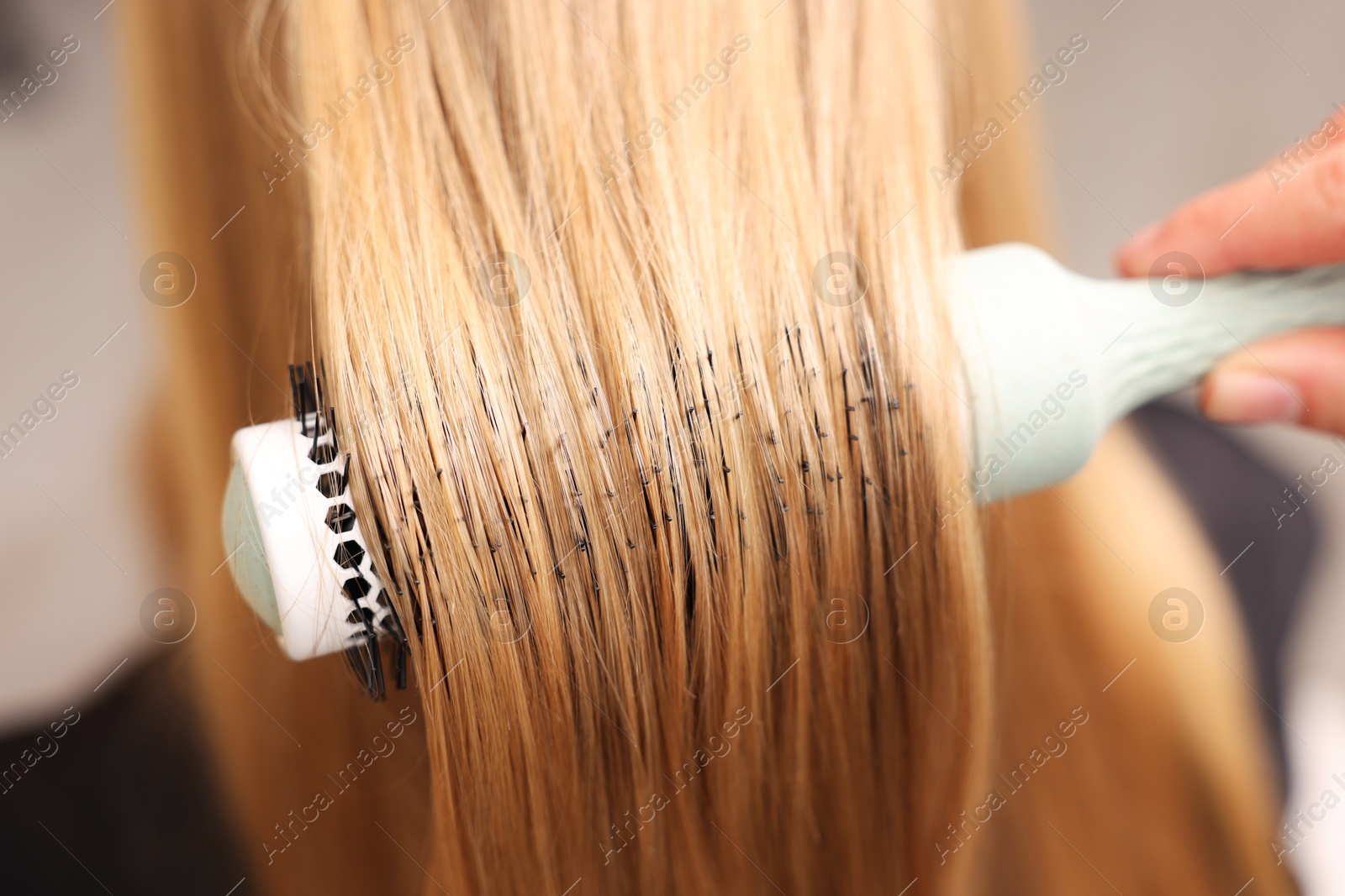 Photo of Hairdresser styling client's hair with round brush in salon, closeup