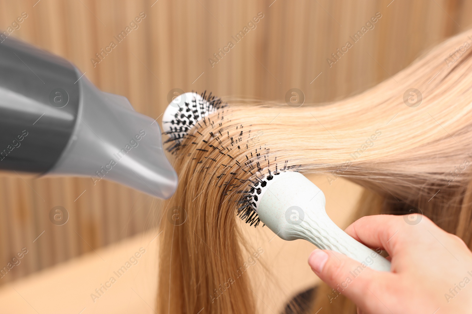 Photo of Hairdresser styling client's hair with round brush and hairdryer in salon, closeup