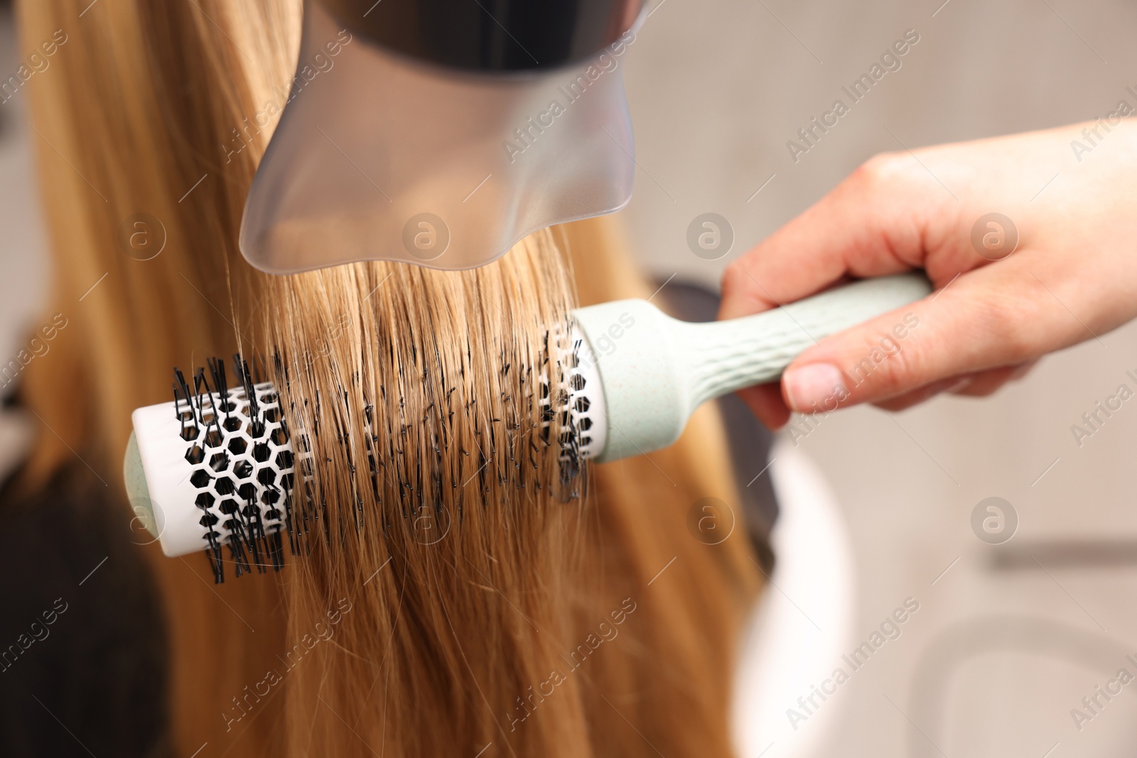 Photo of Hairdresser styling client's hair with round brush and hairdryer in salon, closeup