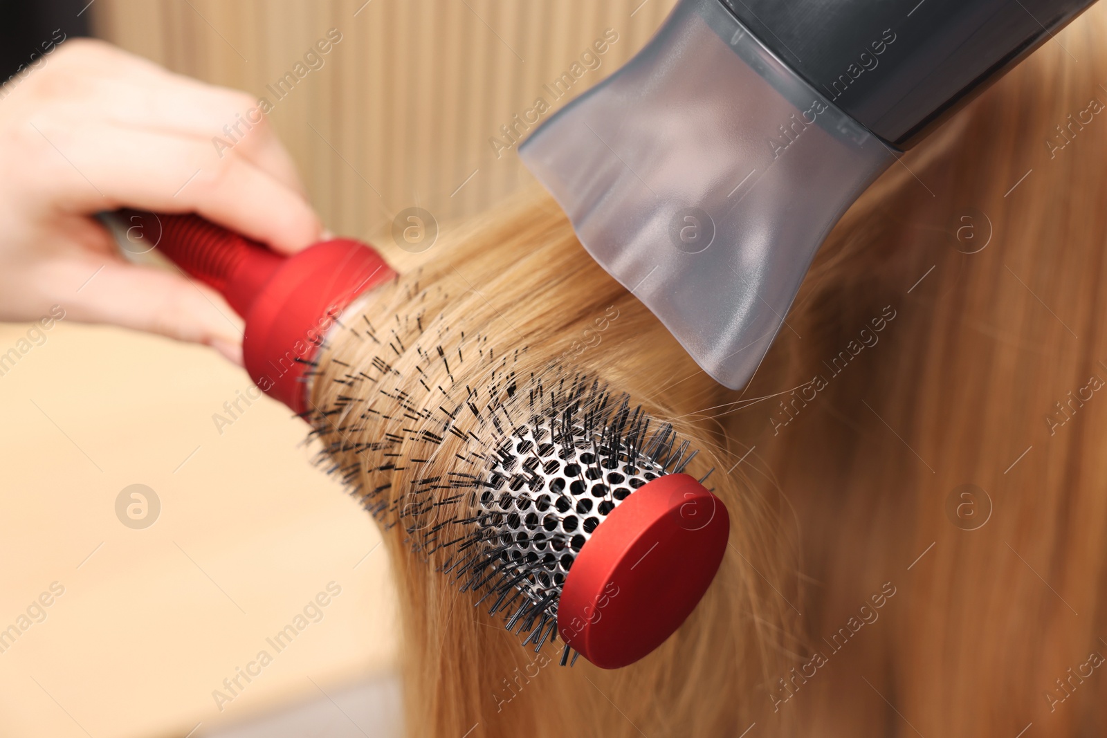 Photo of Hairdresser styling client's hair with round brush and hairdryer in salon, closeup