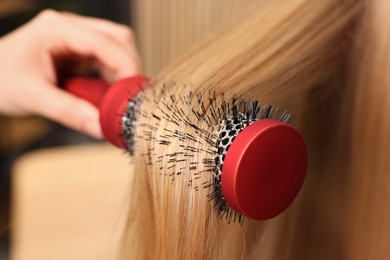 Photo of Hairdresser styling client's hair with round brush in salon, closeup