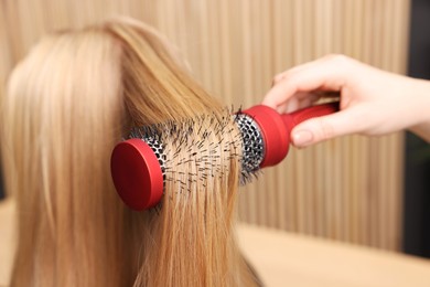 Photo of Hairdresser styling client's hair with round brush in salon, closeup