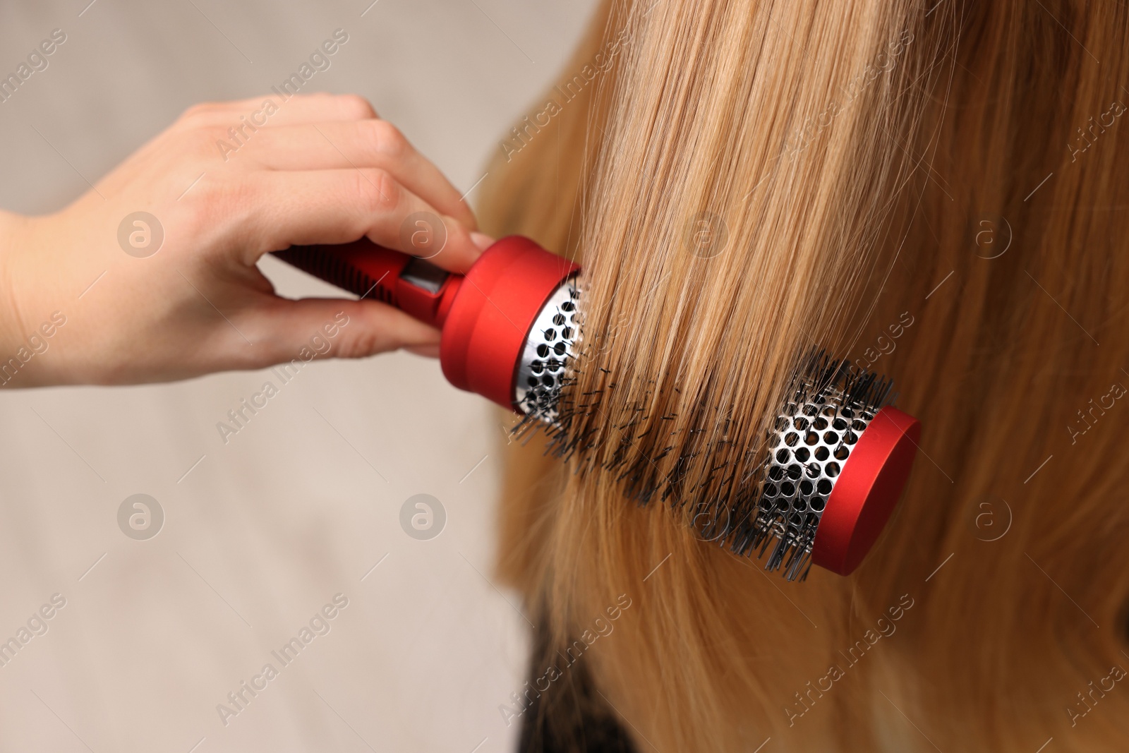 Photo of Hairdresser styling client's hair with round brush in salon, closeup