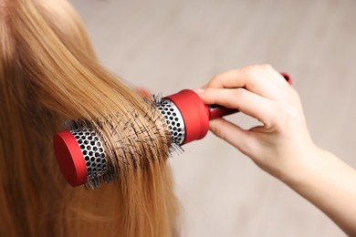 Photo of Hairdresser styling client's hair with round brush in salon, closeup