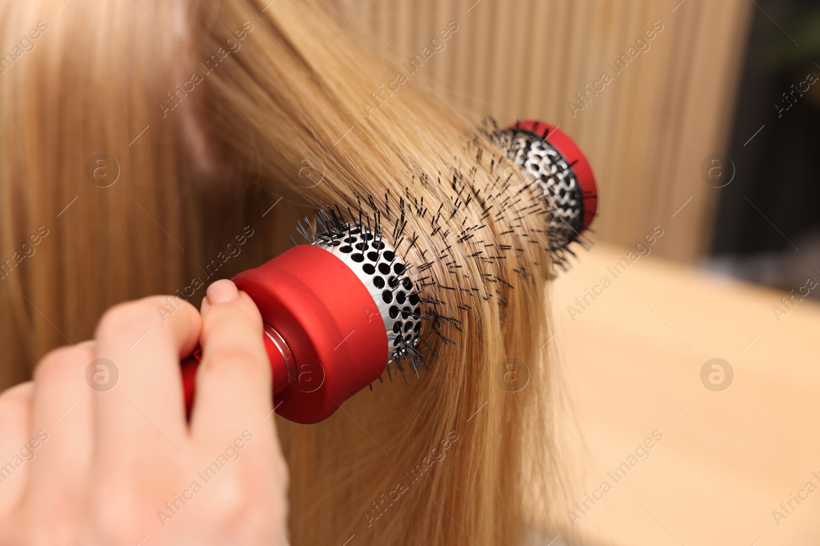 Photo of Hairdresser styling client's hair with round brush in salon, closeup