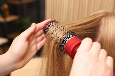 Photo of Hairdresser styling client's hair with round brush in salon, closeup