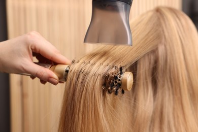 Photo of Hairdresser styling client's hair with round brush in salon, closeup