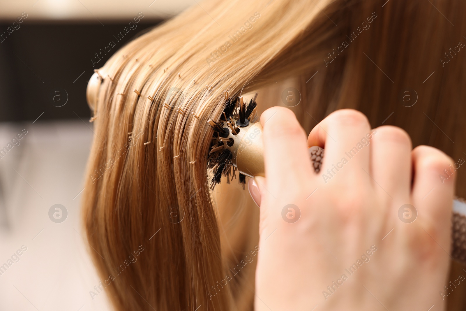 Photo of Hairdresser styling client's hair with round brush in salon, closeup