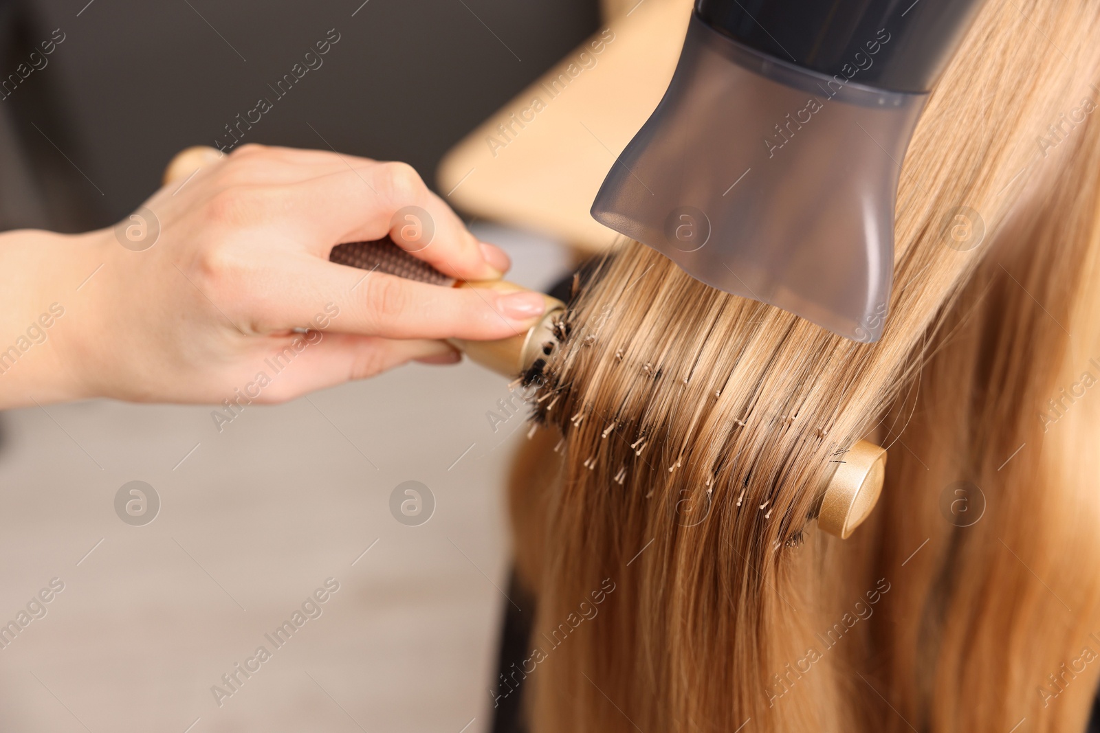 Photo of Hairdresser styling client's hair with round brush in salon, closeup