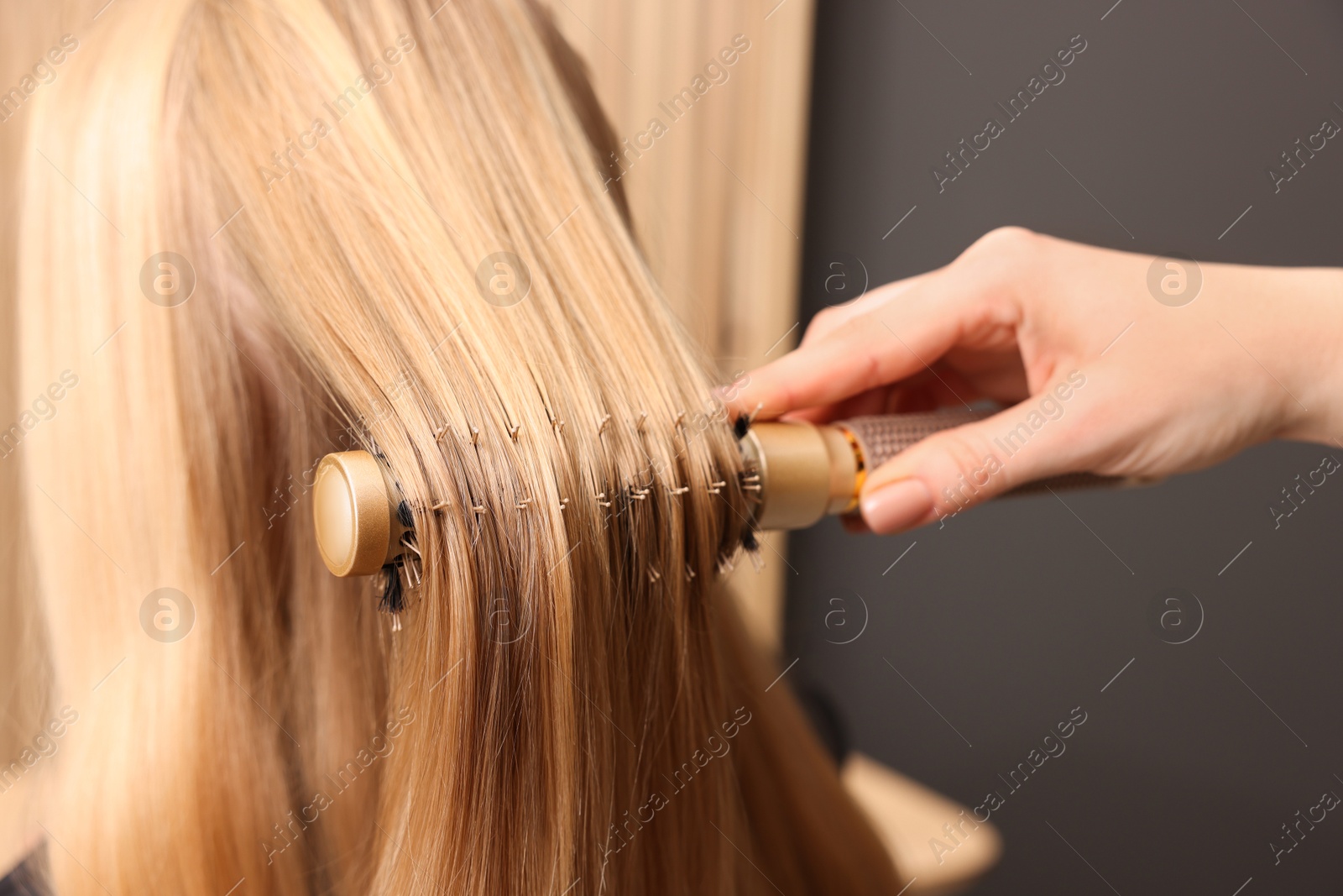 Photo of Hairdresser styling client's hair with round brush in salon, closeup