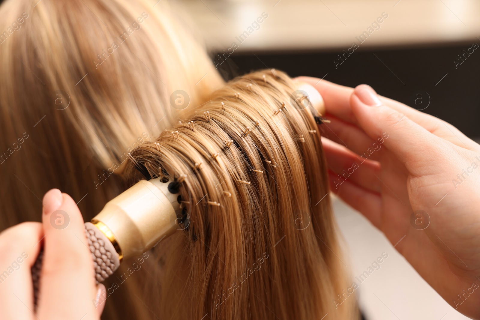 Photo of Hairdresser styling client's hair with round brush in salon, closeup