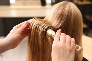 Photo of Hairdresser styling client's hair with round brush in salon, closeup