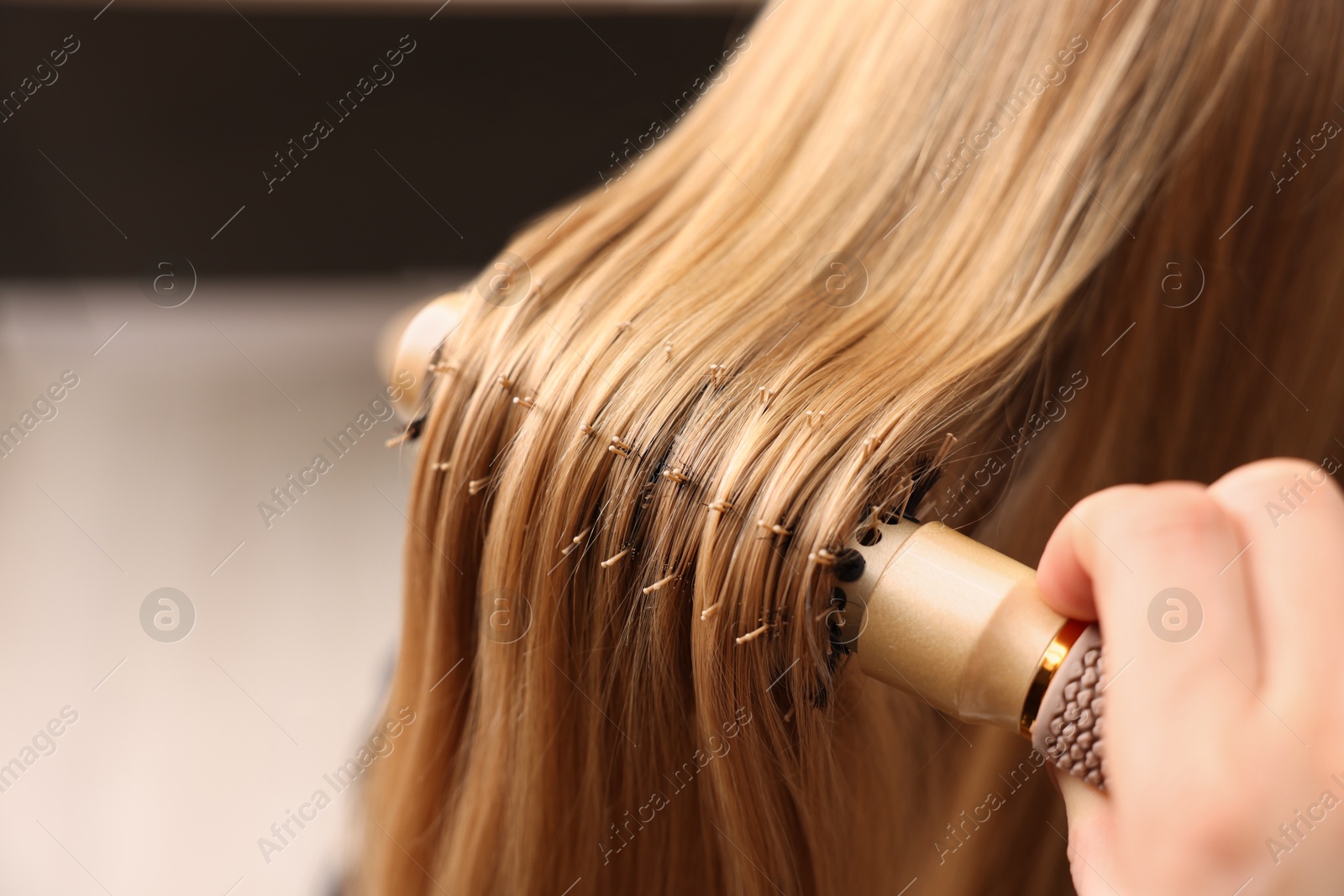 Photo of Hairdresser styling client's hair with round brush in salon, closeup