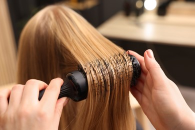 Photo of Hairdresser styling client's hair with round brush in salon, closeup