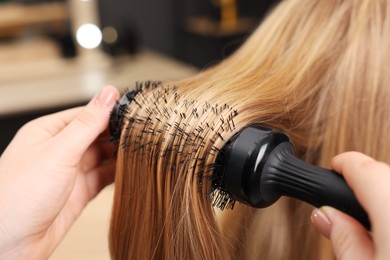 Photo of Hairdresser styling client's hair with round brush in salon, closeup