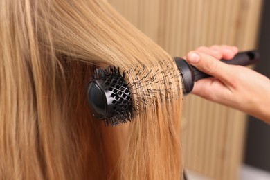 Photo of Hairdresser styling client's hair with round brush in salon, closeup