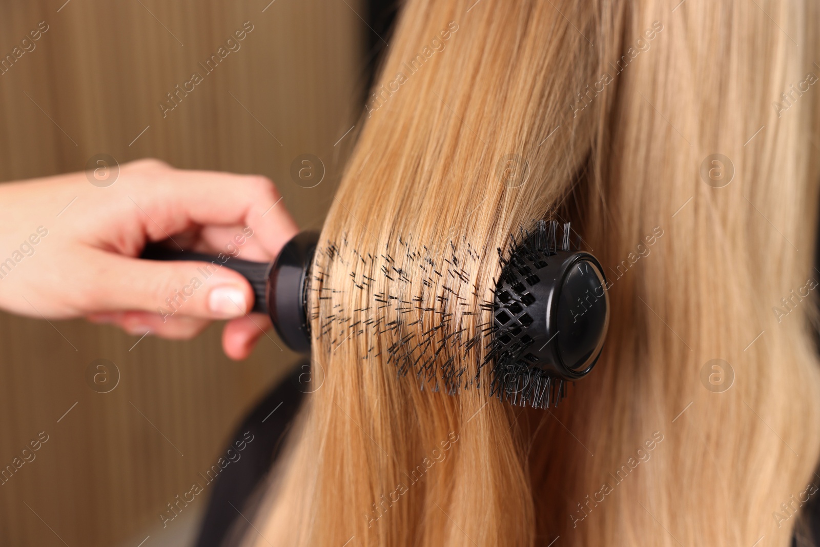 Photo of Hairdresser styling client's hair with round brush in salon, closeup