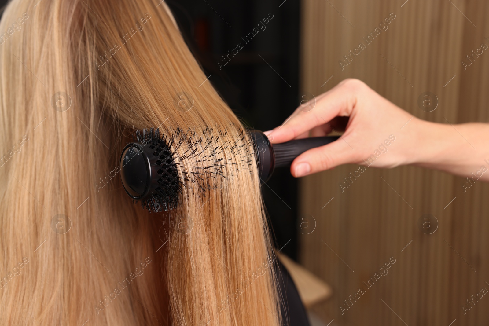 Photo of Hairdresser styling client's hair with round brush in salon, closeup