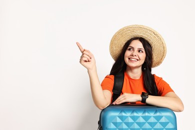 Photo of Young tourist in hat with suitcase pointing at something on white background, space for text